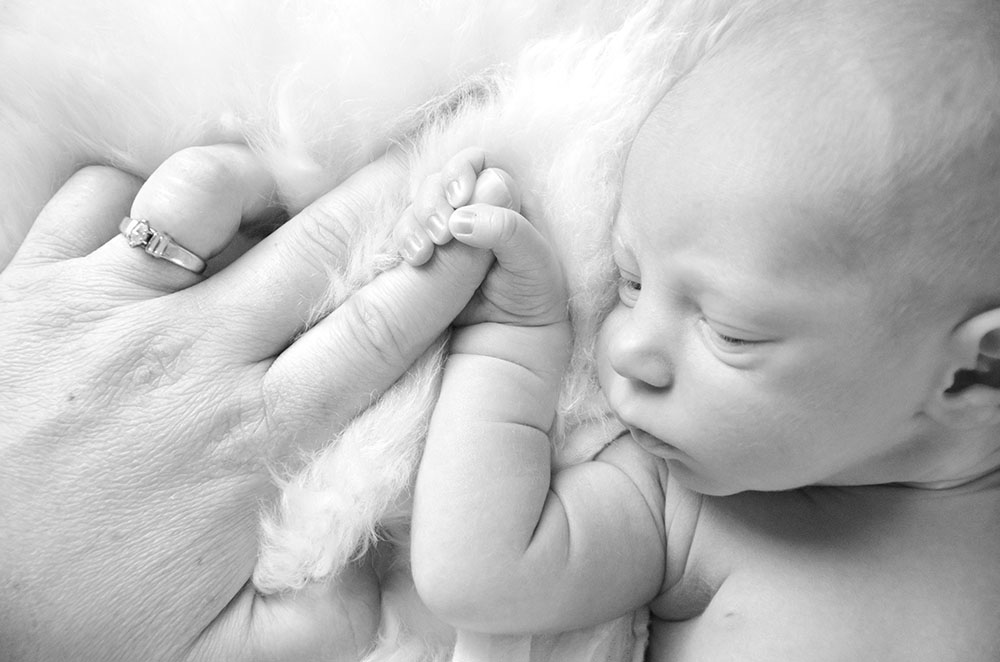 Tiny NICU baby hand held by parent during newborn portrait session.